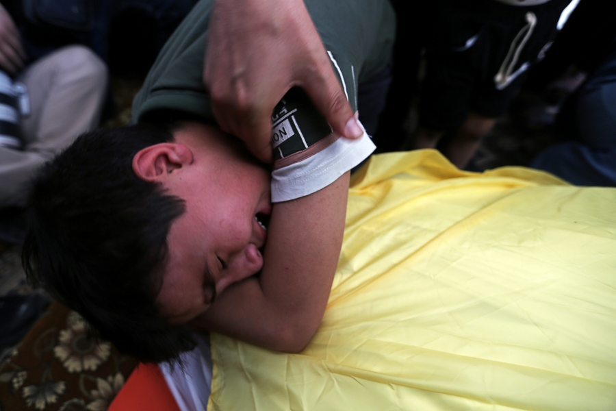 A boy sobs over the covered body of his father A boy sobs over the covered body of his father as a hand holds the boys shoulder.
