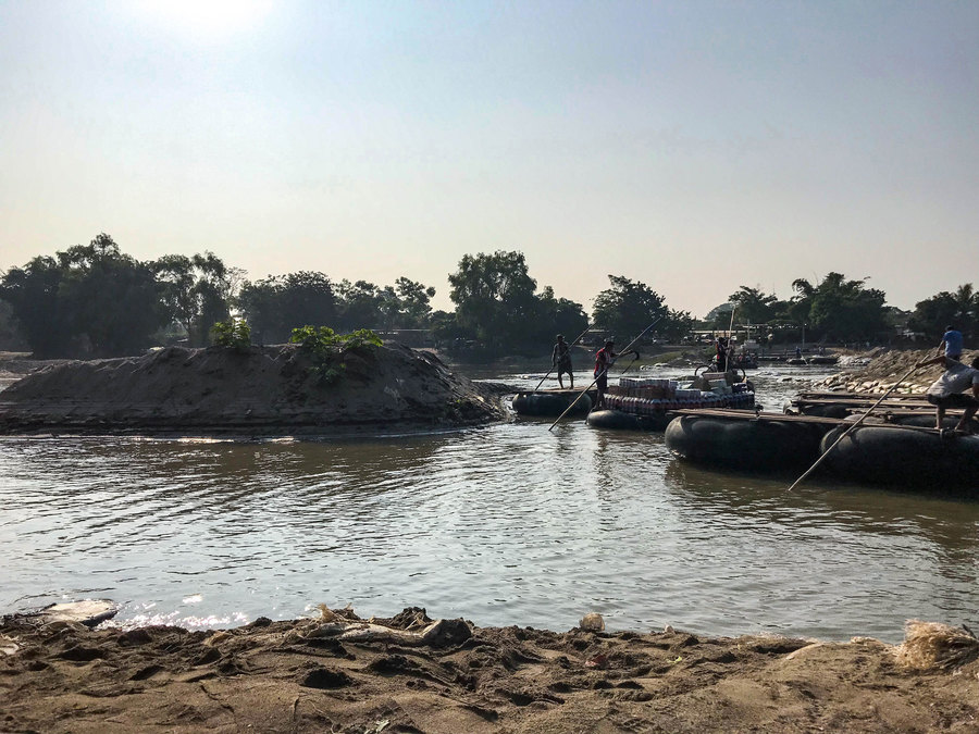 Starting before sunrise and continuing past nightfall, men push rafts of two-by-fours floating on inner tubes. Men are shown on top of rafts with wooden tops on a river.