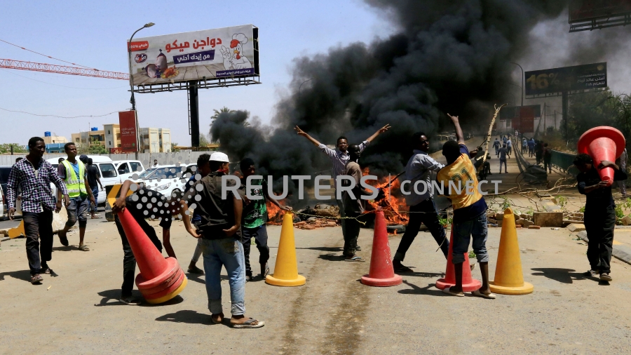 Men and traffic cones are around a tire fire with a plume of black smoke