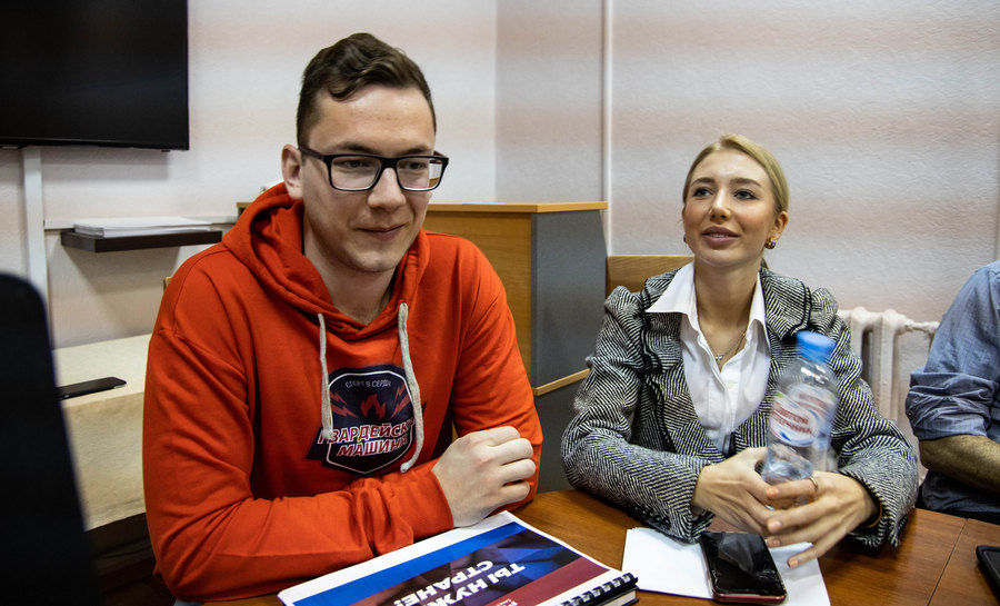 Alexander Malikov, director of the St. Petersburg branch of Molodaya Gvardiya (left) sits at a table with other members at a recent meeting. Alexander Malikov is shown wearing a red hooded sweatshirt while sitting at a table next to a young woman.