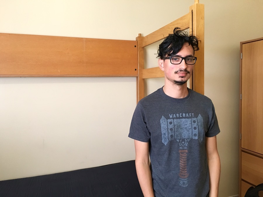 Man stands in front of a bed in a dorm room Man stands in front of a bed in a dorm room
