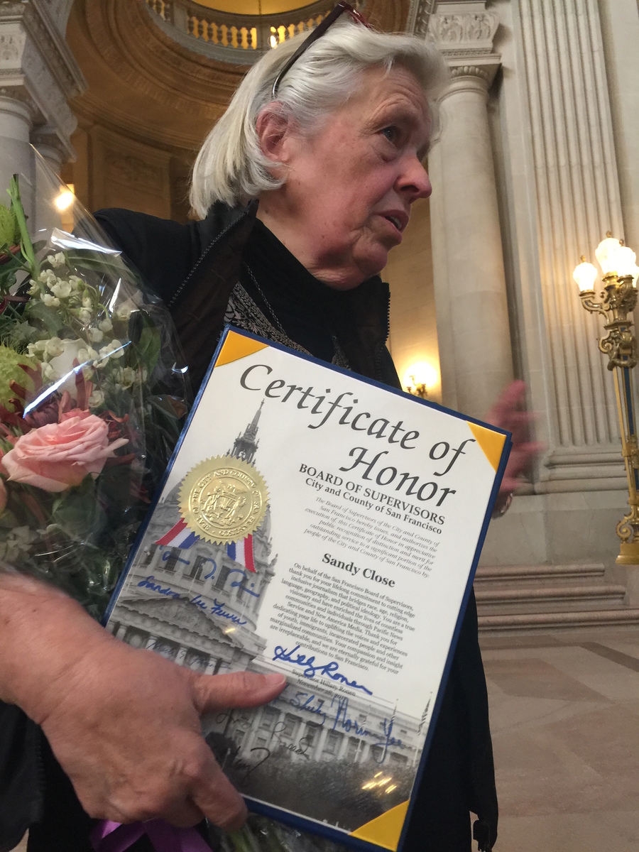 Woman stands with certificate, flowers behind