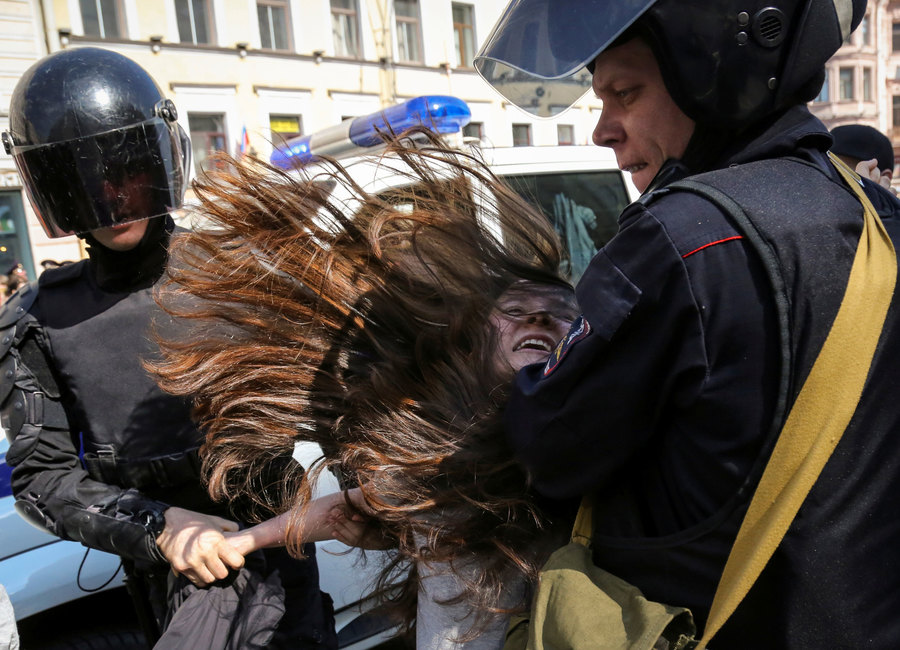 Police officers detain an opposition protester during a May Day rally in Saint Petersburg, Russia May 1, 2019. Two Russian police officers are shown with helmets and dark visors holding a woman who is resisting.