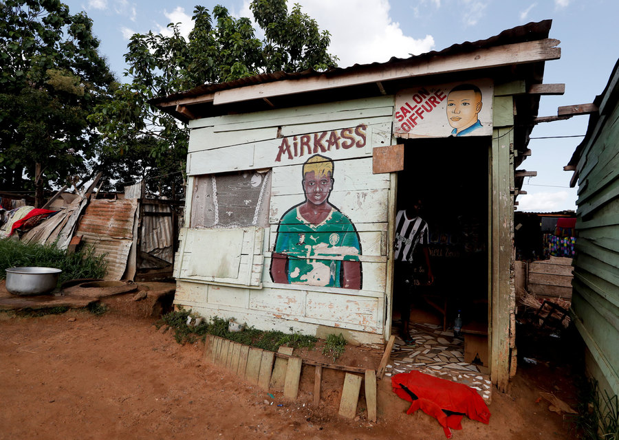 Gaelle Enganamouit is depicted on the facade of a hairdressers' shop. A small wooden building is shown with a painting of a soccer player on the wall.