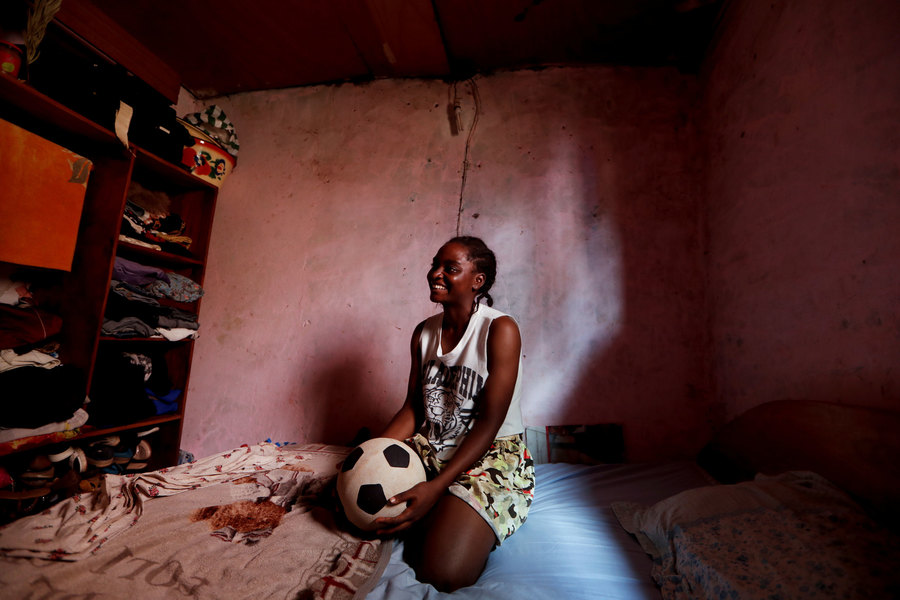 Pouadjeu sits on her bed. A young woman is shown sitting on her bed holding a soccer ball.