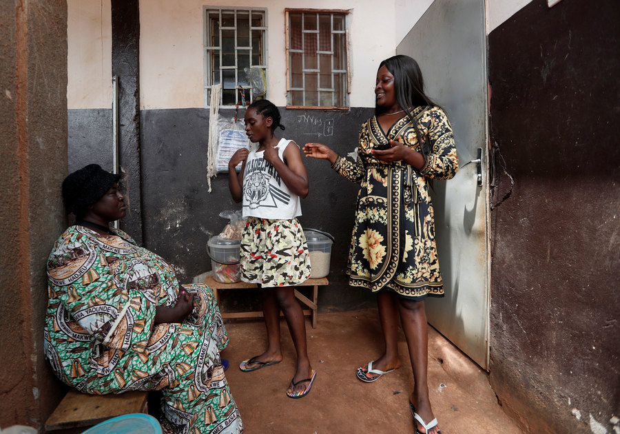 Pouadjeu and her aunt Rosalie Tchamkou and her sister Kevine at their house. Two older woman — one seated — are shown on either side of a younger woman wearing a shirt with the word Philadelphia on it.