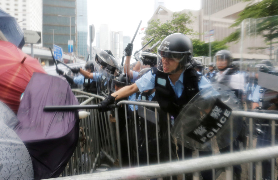 Protesters clash with riot police during a demonstration near the Legislative Council in Hong Kong, China, June 12, 2019. A police officer is shown with a helmet and clear face mask down, striking a person with an umbrella with his batton.