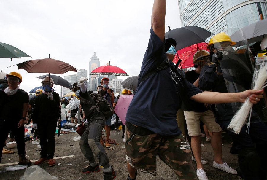 Protesters wearing masks and holding umbrellas take part in a demonstration in Hong Kong, China, June 12, 2019. Several potesters are shown wearing masks and holding umbrellas with one person center frame who is about to throw and object.
