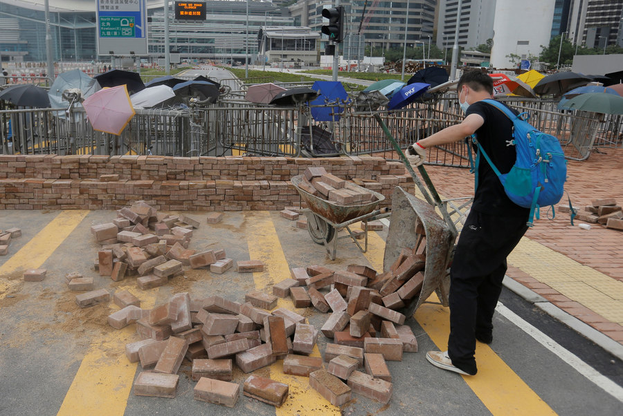 A protester gathers bricks to build a barricade during a demonstration near the Legislative Council in Hong Kong, China, June 12, 2019. A man is shown wearing a blue backpack and dumping out a wheelbarrow of bricks onto the street.