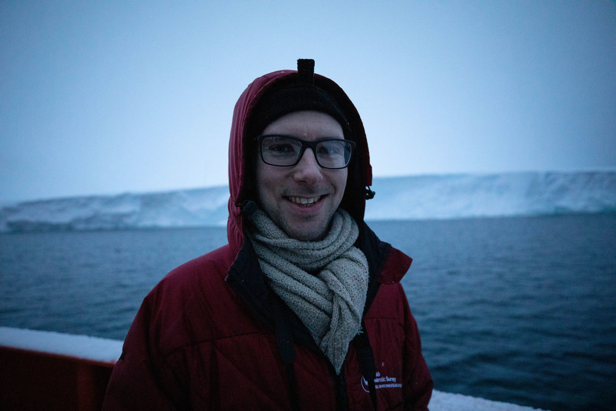 Peter Sheehan, an oceanographer at the University of East Anglia, in front of Thwaites Glacier early on the morning of the Nathaniel B. Palmer's arrival. Oceanographer Peter Sheehan is shown with a red jacket and white scarf with Thwaites glacier in the background.