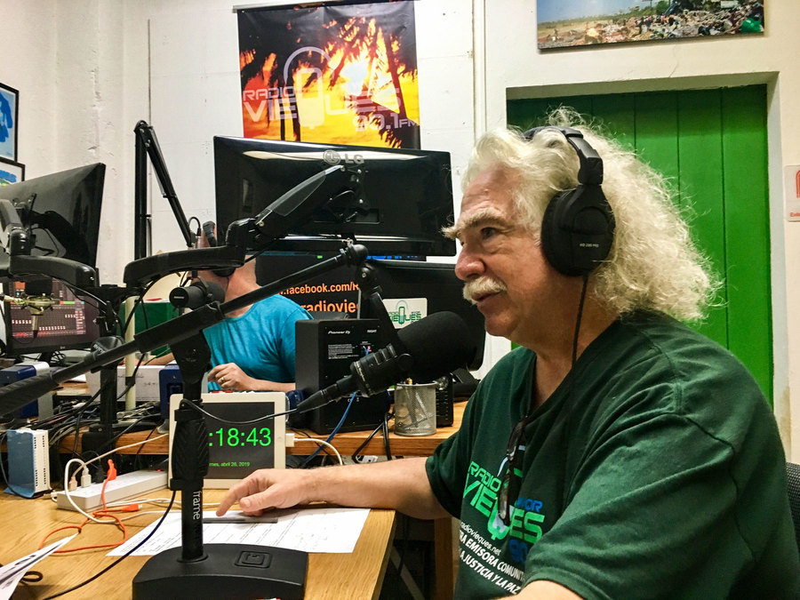 Local resident Robert Rabin on the air with Radio Vieques. A man is shown sitting in front of a microphone with headphones on and wearing a green shirt.