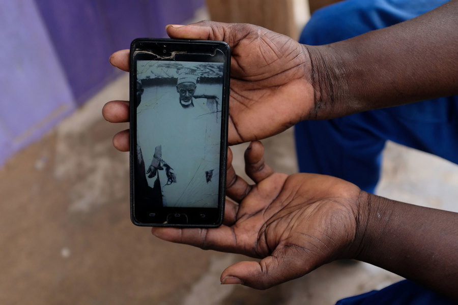 Shaibu shows a photograph of his grandfather. A mobile phone with a black and white photograph displayed is shown held by two hands.