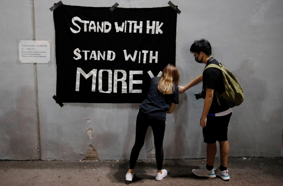 A young woman and a young man hang a banner reading "Stand with HK/Stand with Morey"