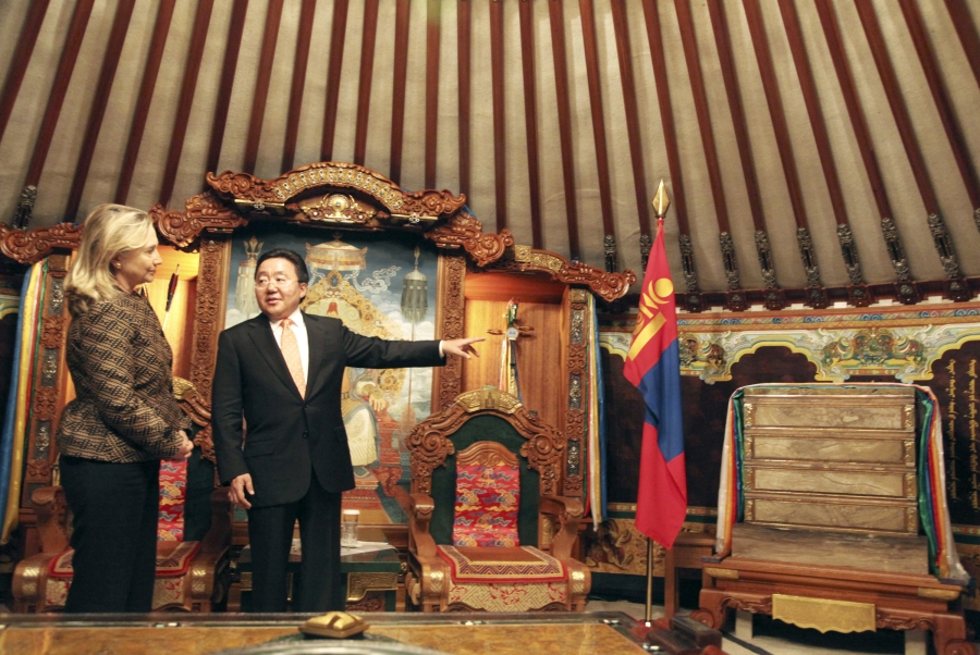 A man gestures toward a flag and ornate furnitures as a woman looks on.