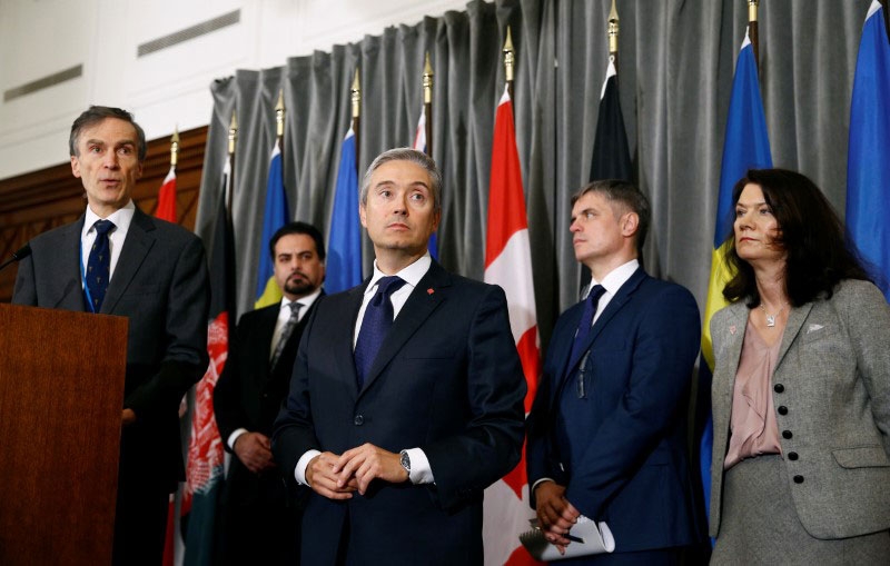 Ministers after a meeting of the International Coordination and Response Group Several people stand in suits in front of flags.