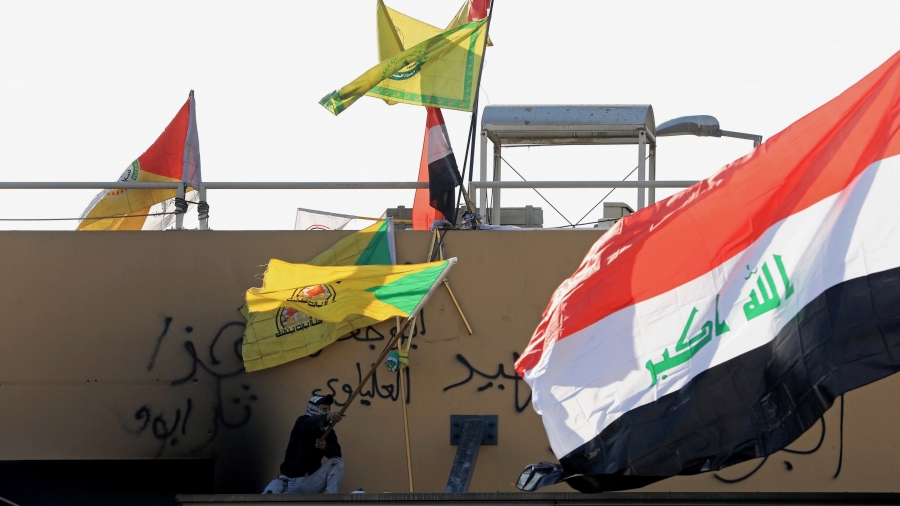 A member of Hashd al-Shaabi waves a flag of Kataib Hezbollah militia group during a protest to condemn air strikes on bases belonging to Hashd al-Shaabi (paramilitary forces), outside the US Embassy in Baghdad, Iraq, Jan. 1, 2020. A member of Hashd al-Shaabi waves a flag