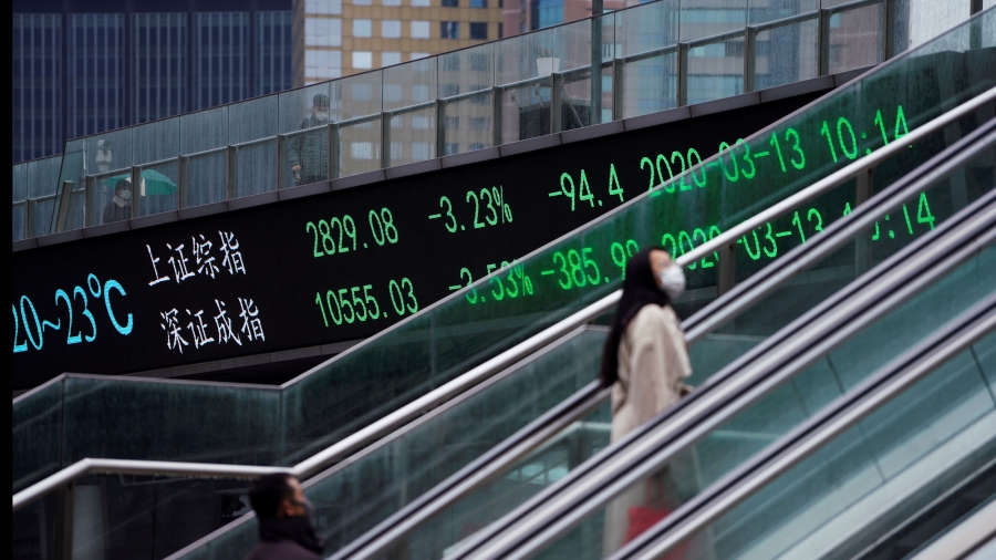 Pedestrians wearing face masks ride an escalator near an overpass with an electronic board showing the Shanghai and Shenzhen stock indexes, following an outbreak of the novel coronavirus in the country, in Shanghai, China. A woman is shown wearing a khaki coat and a face mask while riding an escalator upward.