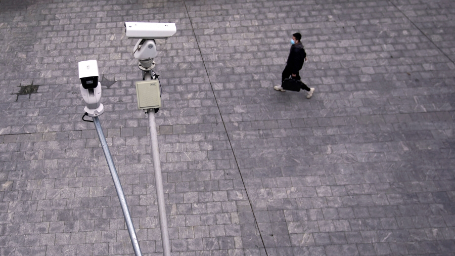 A man wearing a protective mask walks under surveillance cameras in Shanghai, China, as the country is hit by a novel coronavirus outbreak. Two surveillance cameras are shown in the nearground with a man walking in a stone walkway and wearing a protective face mask in the distance.