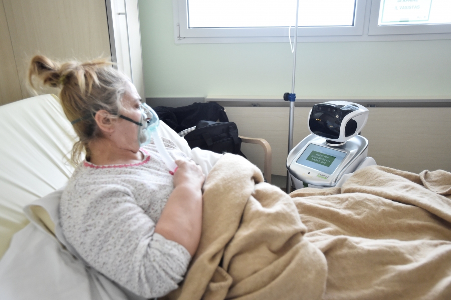 Tommy the robot interacts with a COVID-19 patient. A sick woman looks at a robot from her hospital bed.