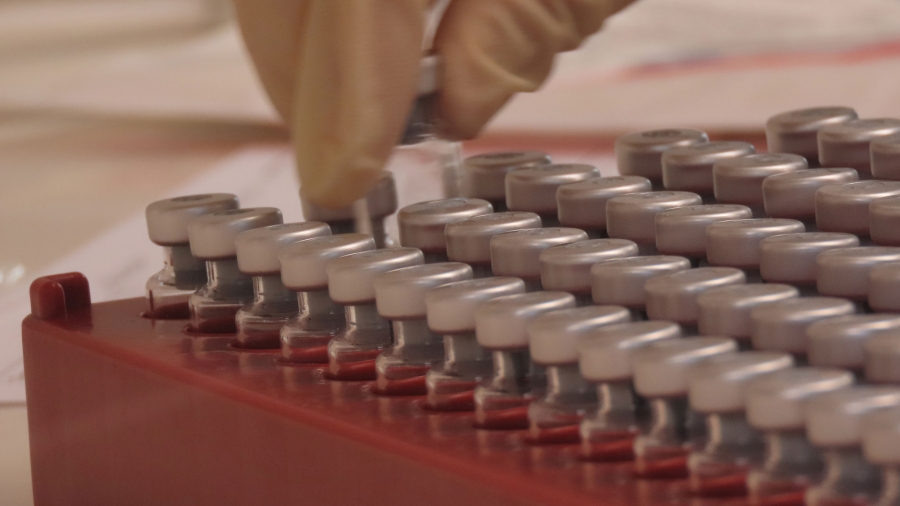 Vaccine vials undergo quality control at the Clinical Biomanufacturing Facility in Oxford, Britain, April 2, 2020. A red tray of dozens of vials is shown with a hand picking one of the vials up.