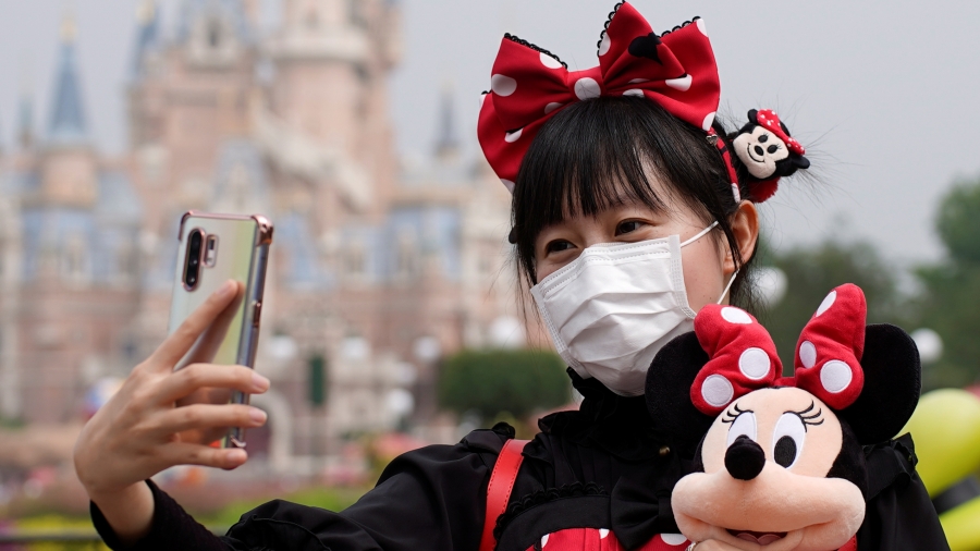 A visitor dressed as a Disney character takes a selfie while wearing a protective face mask at Shanghai Disney Resort as the Shanghai Disneyland theme park reopens following a shutdown due to the coronavirus disease (COVID-19) outbreak, in Shanghai, China A young woman wears a red bow and holds a doll as she takes a selfie at Disneyland in Shanghai
