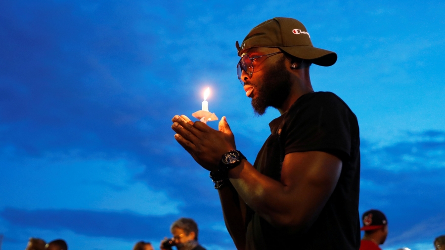 A man holds a candle in commemoration of George Floyd, a black man killed while in Minneapolis police custody, in Minneapolis, Minnesota, June 3, 2020. A man is shown wearing a dark shirt and baseball hat backwards while holding a small candle.
