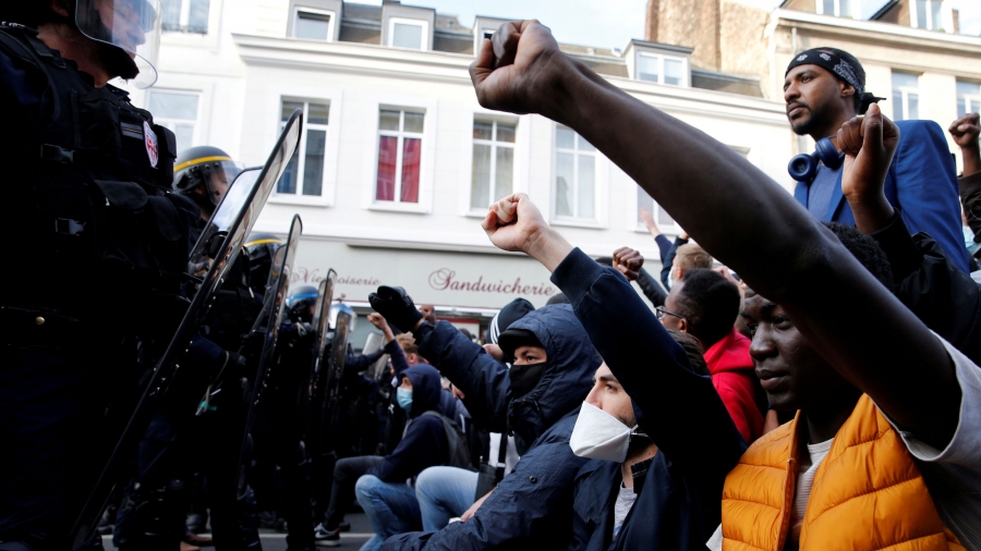 Protesters raise their fists during a demonstration in memory of Adama Traoré, a 24-year-old black Frenchman who died in a 2016 police operation which some have likened to the death of George Floyd in the United States, on the Place de la Republique in Li A large group of demonstrators are shown kneeling with their fists in the air opposite a row of police carrying large shields.