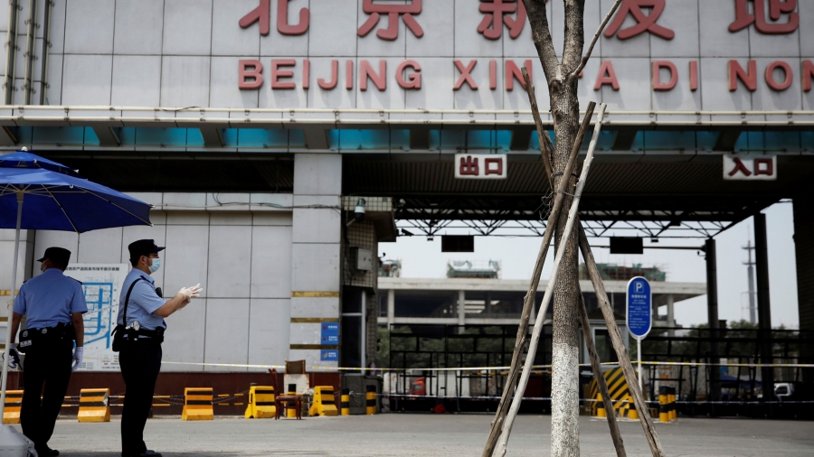 Police officers wearing face masks and gloves stand guard outside an entrance to the Xinfadi wholesale market, which has been closed following cases of coronavirus infections, in Beijing, China, June 16, 2020. Two police officers are shown wearing protective face masks with the empty entrance to a food market in the background.