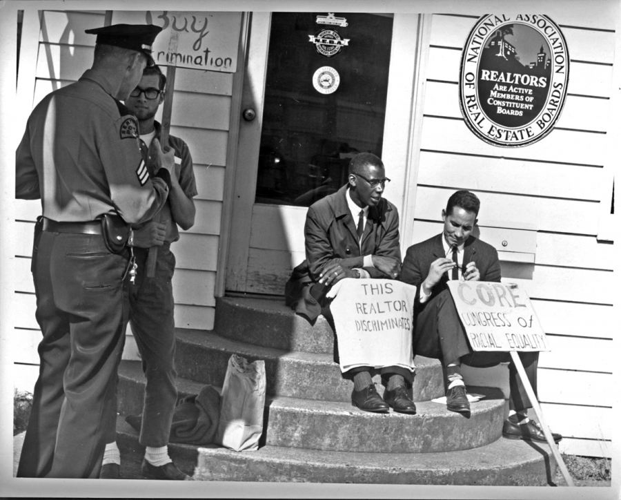 Fair housing protest, 1964, Seattle, Washington, United States. Two black men sit on steps with two white police offers standing by them.