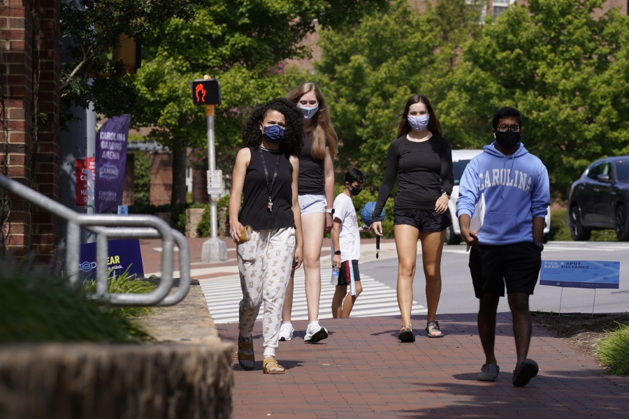 Several universities cancelled in-person classes after a spike in cases. College students walking, wearing masks.