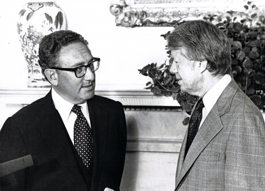 Two very different approaches to foreign policy: Kissinger and Carter. Two men face each other, presumably speaking to each other.
