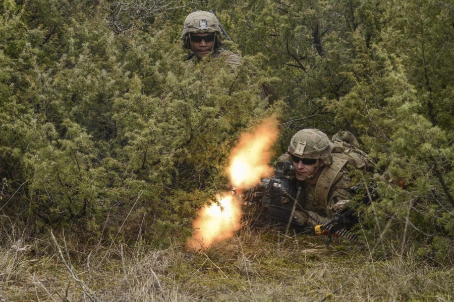 U.S. soldiers train with Hungarian armed forces on March 3, 2020. Army Staff Sgt. Two soldiers hunch down in a bush. The photo displays the bullets from one of the guns mid-fire.