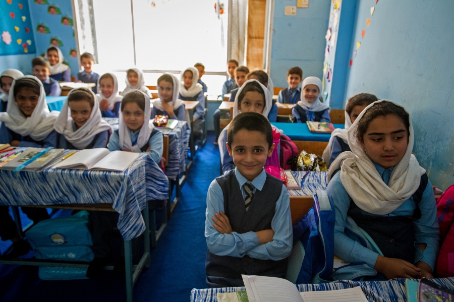 A coed private school classroom in Kabul, September 2019. Girls’ education is still restricted in Taliban-controlled areas. A group of children in a classroom smile for the camera while sitting at their desks.