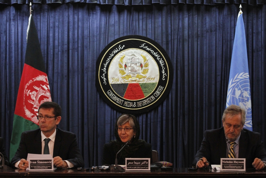 The Afghan women’s rights advocate Sima Samar, center, at a United Nations event on domestic violence in Afghanistan in 2015. Three people sit side by side at a table. Behind them is the national flag of Afghanistan and the flag of the United Nations.