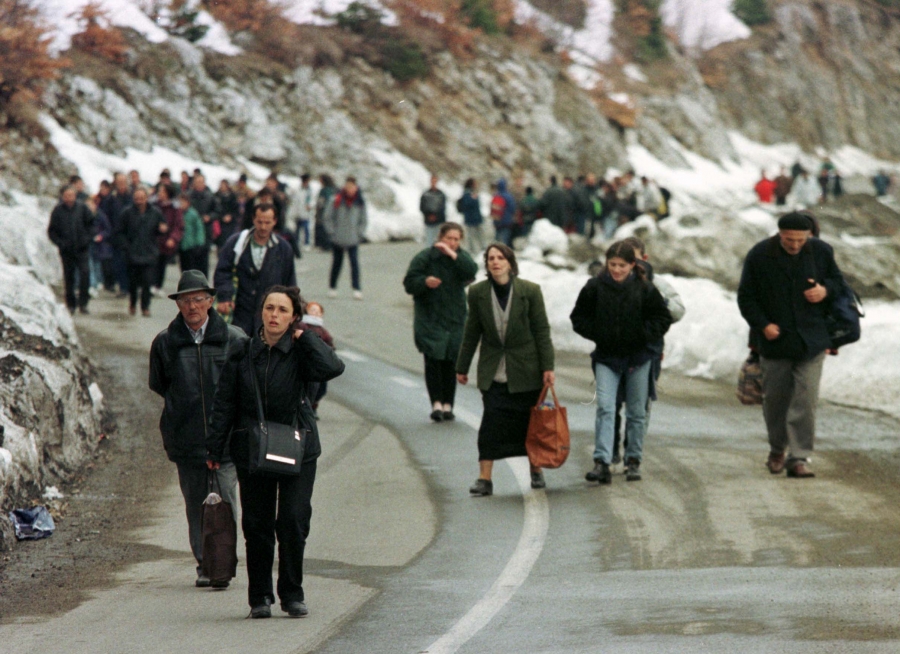 Refugees from Kosovo cross the mountains on foot to reach Montenegro in 1999. A large group of people walking on a mountainside road.