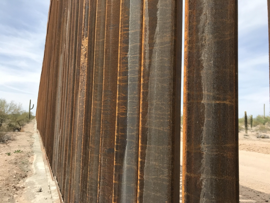 Migrants face challenges when trying to cross the border into the US A view from the Mexican side of a 30-foot border wall, peeking through the slabs to show the US side of the border.