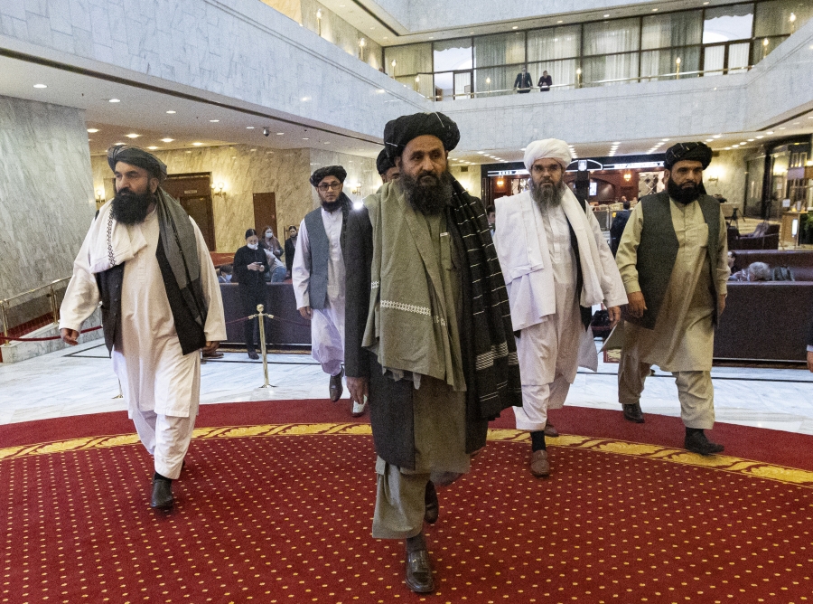 A Taliban delegation arrives for a conference in Moscow A group of men wearing Afghan traditional clothes walk across a reddish carpet in a lobby.