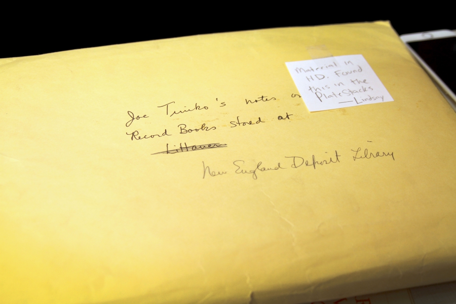 A yellow manila envelope has a Post-it it that says "Found this in the plate stacks - Lindsay" and the name a library crossed out and replaced with "New England Deposit Library."