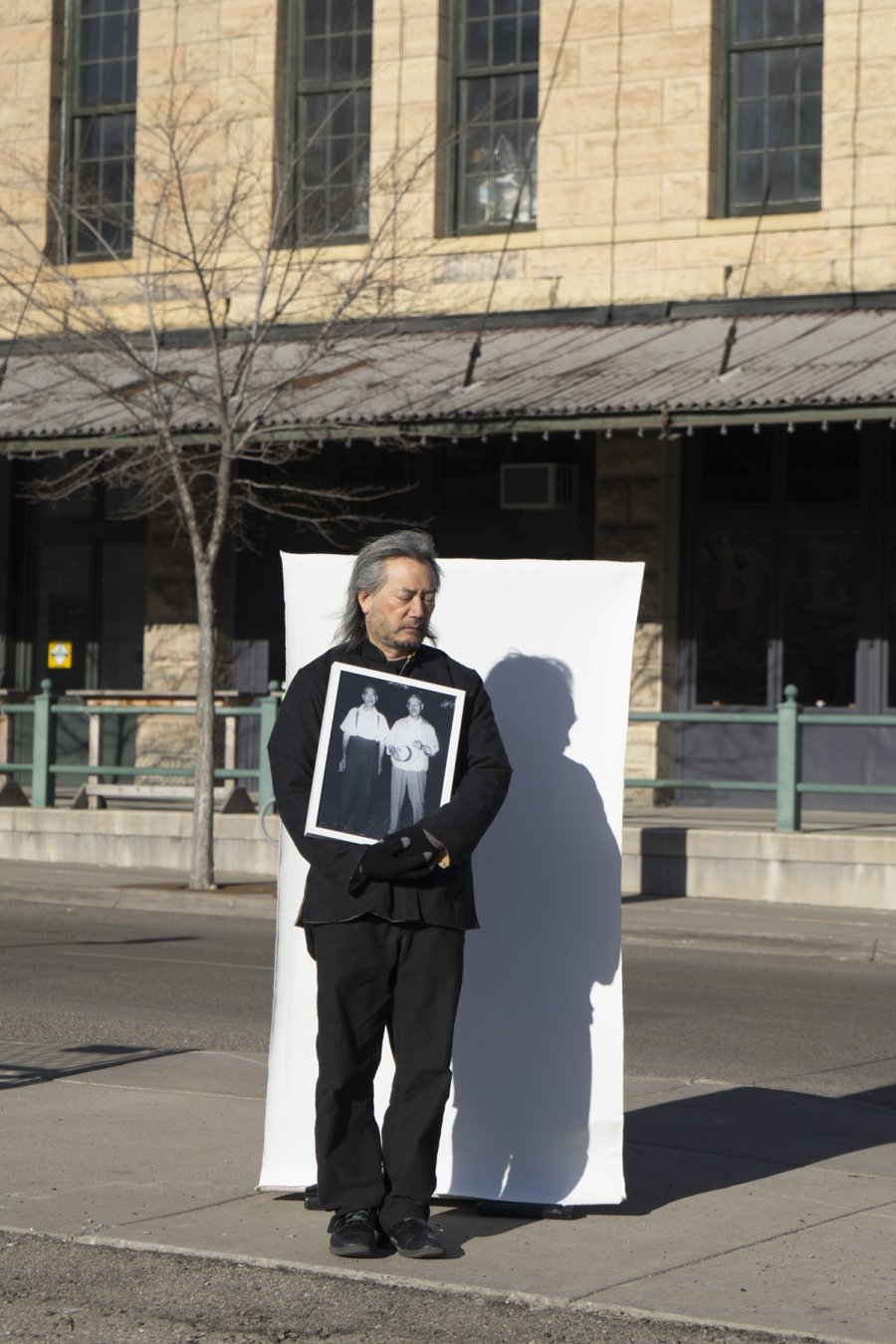 A man stands outside holding a photograph in front of a white sheet
