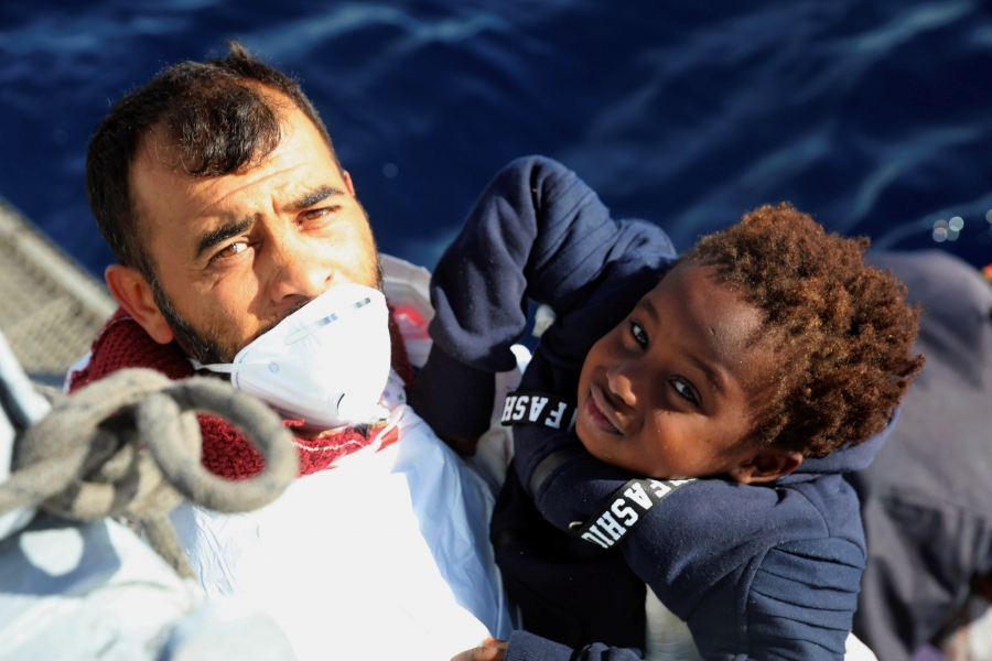 Libyan coast guard rescues a migrant child in the Mediterranean Sea. Man on a boat lifting a young child to hand to rescuers