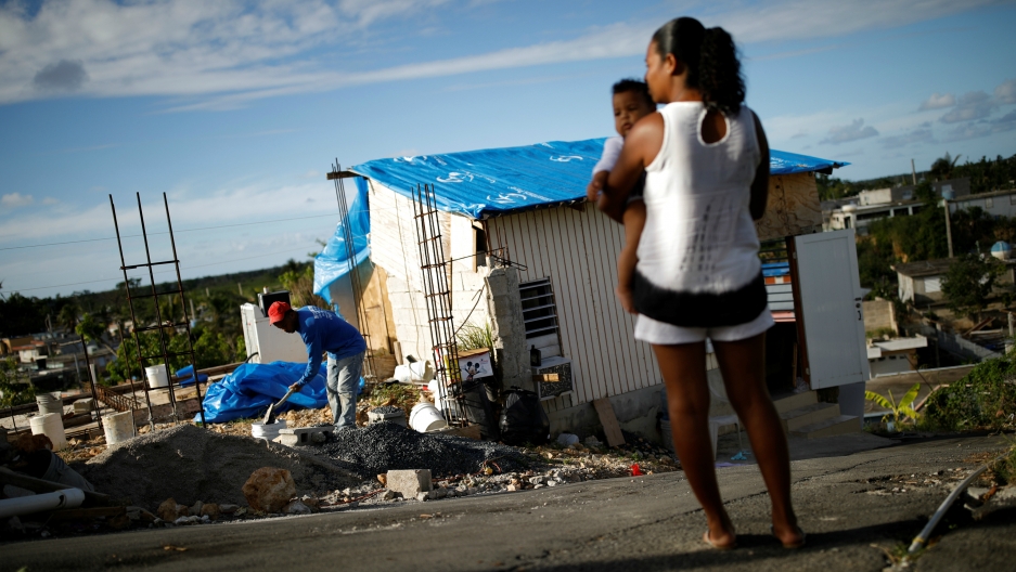 Samuel Vasquez rebuilds his house, which was partially destroyed by Hurricane Maria, while his wife, Ysamar Figueroa, looks on in Canovanas, Puerto Rico, Dec. 11, 2017. Puerto Rico is once again bracing for hurricane season, just as a new study has found