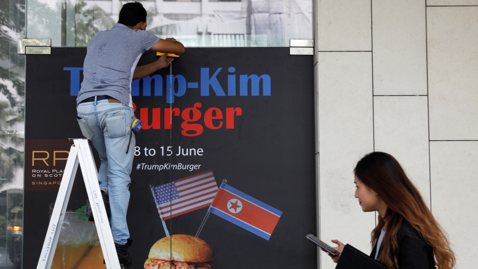 A worker puts up an advertisement for the Trump-Kim burger, at Royal Plaza on Scotts hotel in Singapore, June 7, 2018. A worker in blue jeans, stands on a ladder and puts up an advertisement for the Trump-Kim burger.