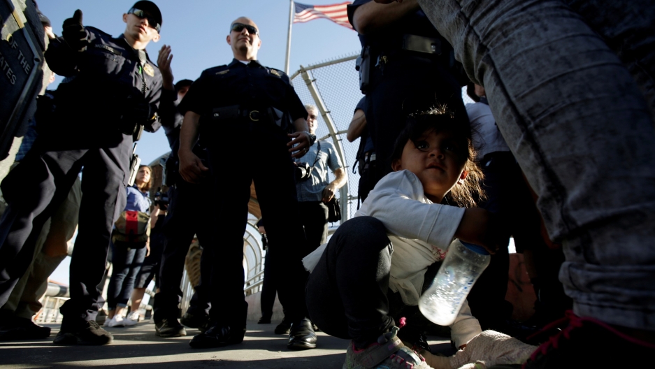 Migrant families from Mexico listen to officers of the US Customs and Border Protection before entering the United States to apply for asylum at Paso del Norte international border crossing bridge in Ciudad Juarez, Mexico, June 20, 2018. A you migrant girl crouches next to her family as they listen to officers of the US Customs and Border Protection before entering the United States to apply for asylum.