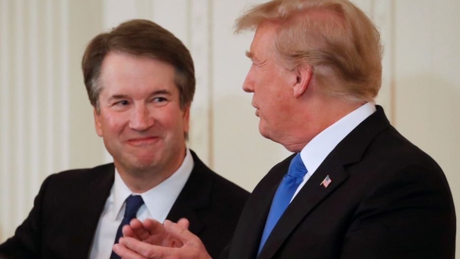 President Donald Trump and his nominee for the US Supreme Court, Brett Kavanaugh, talk during an announcement event in the East Room of the White House. President Donald Trump is shown standing in the nearground clapping his hands with his nominee for the US Supreme Court, Brett Kavanaugh smiling in the background.