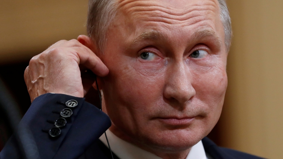 Russian President Vladimir Putin listens as US President Donald Trump speaks during their news conference in Helsinki, July 16, 2018. A close-up photography of Russian President Vladimir Putin touching an ear piece.