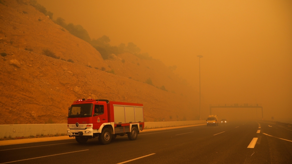 Fire fighters are seen amid smoke as a wildfire burns in Kineta, near Athens, Greece, July 23, 2018. A fire truck drives along a road in Greece amid orange smoke.