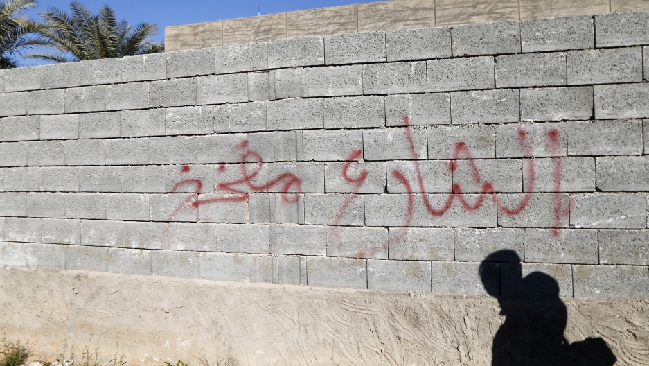 Graffiti warning on a wall saying that the street is mined is seen in the city of Ramadi. Graffiti warning on a brick wall saying that the street is mined with the shadow of a person reflected on it.
