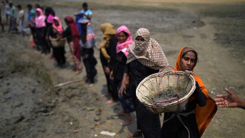 rohingya women lined up, carrying large baskets 