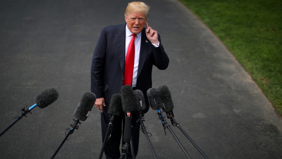 President Donald Trump speaking to the media, May 2018. President Donald Trump is shown with his hand cupping his ear in front of several microphones outside.