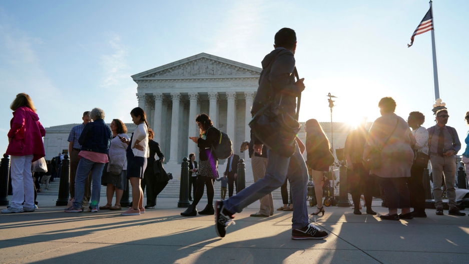 People wait in line to attend the opening day of the new term of the Supreme Court in Washington, October 1, 2018. People are shown waiting in line with the Supreme Court in the background.